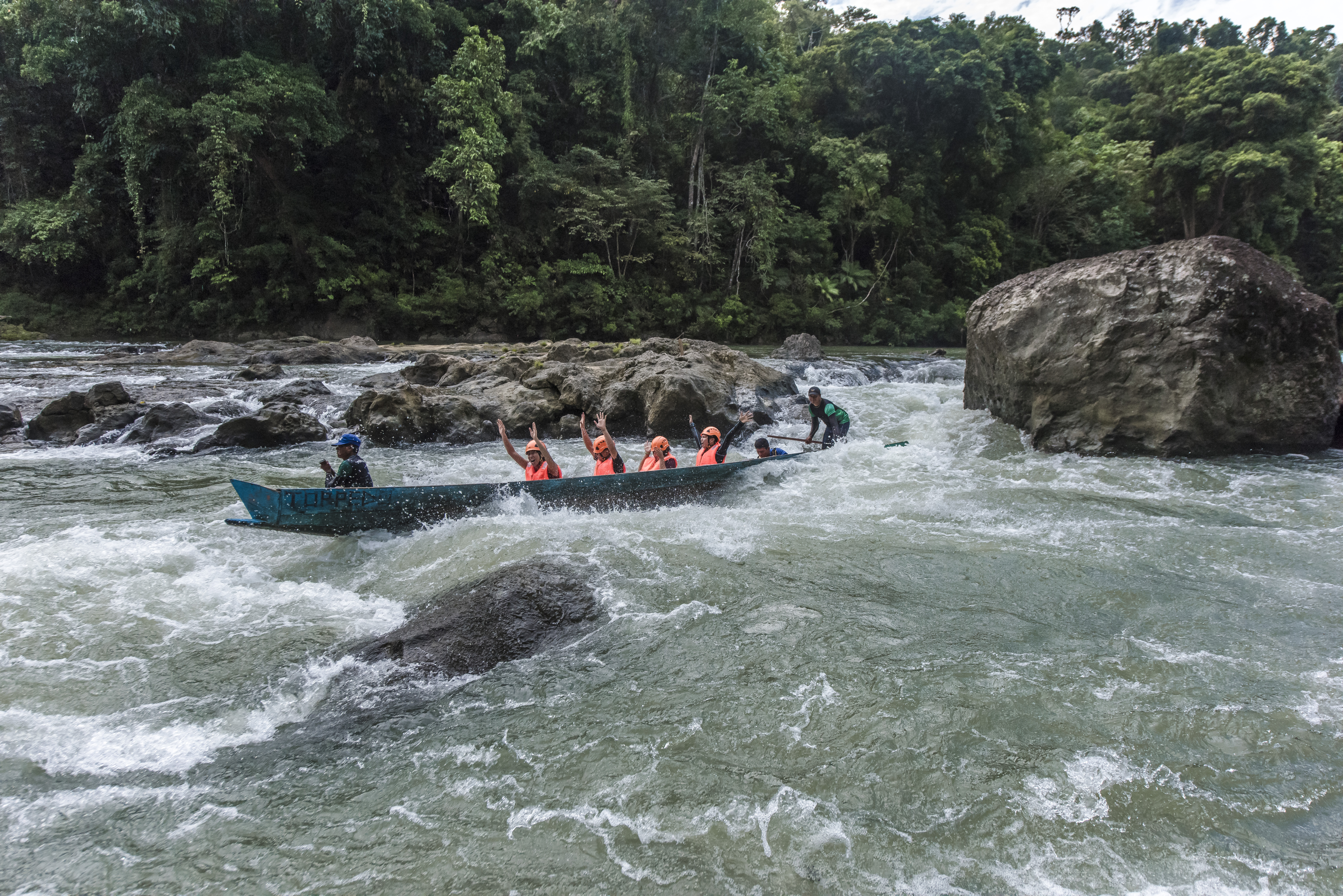 A narrow wooden torpedo boat racing through the emerald jungle waterways of the Ulot River, Samar